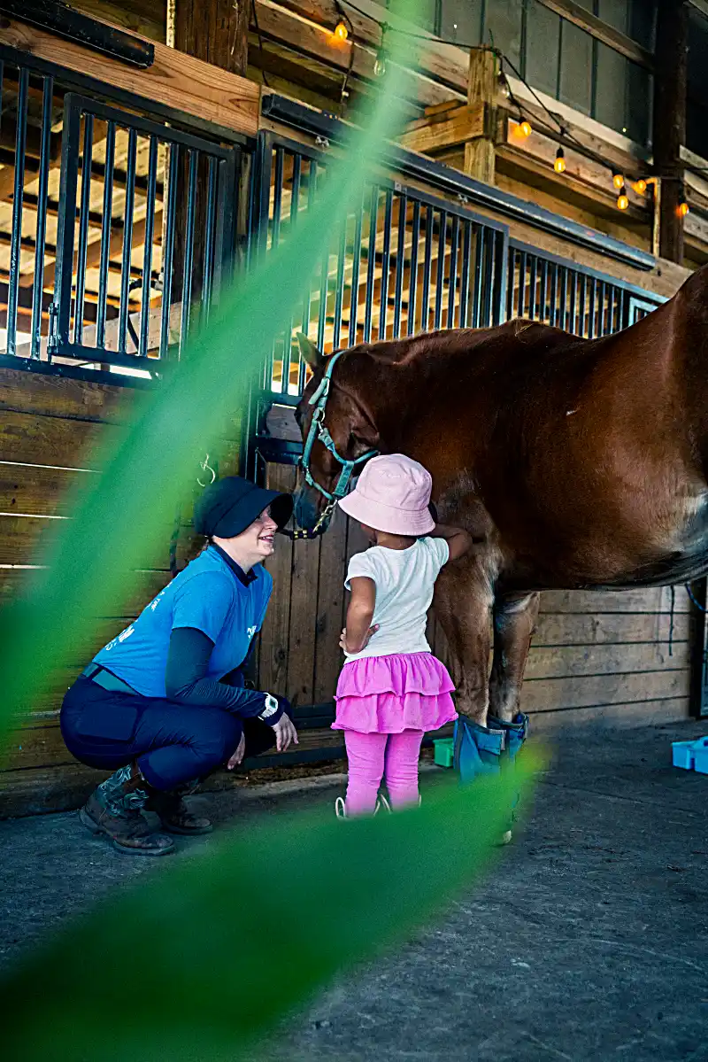 Preschool-age child petting a horse's nose during Tiny Trotters introduction